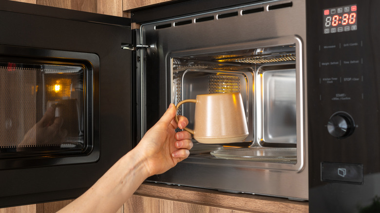 Hand placing coffee mug going in microwave