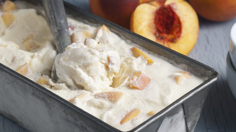 A rectangular tray of homemade peach ice cream with a scoop in the middle