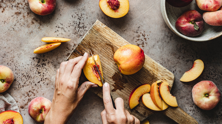 A pair of hands chopping up fresh peaches on a small wood board