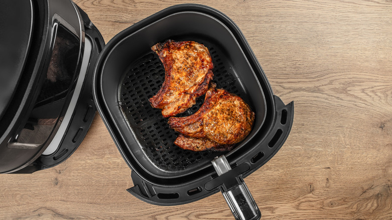 An overhead view of two cooked pork chops in an air fryer basket