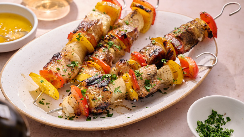 Salmon skewers on a platter with garnishing and honey glaze in dipping bowls on the side