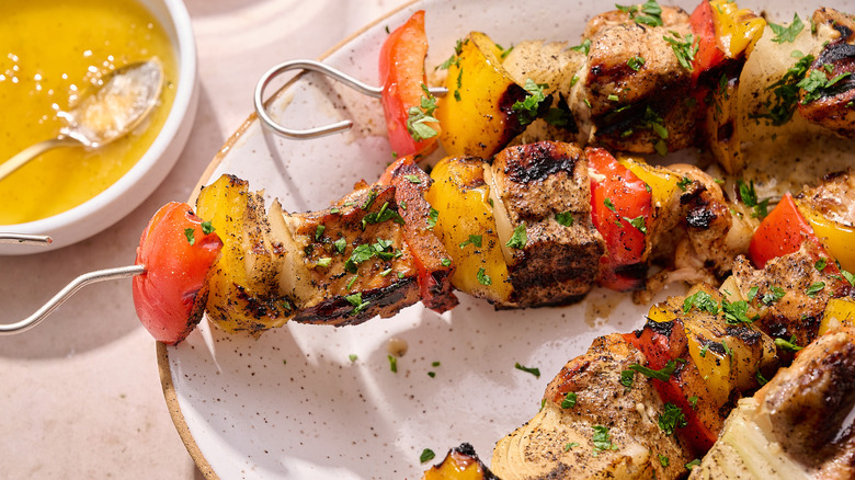Close up of salmon skewers on a platter next to bowl of garlic and honey glaze
