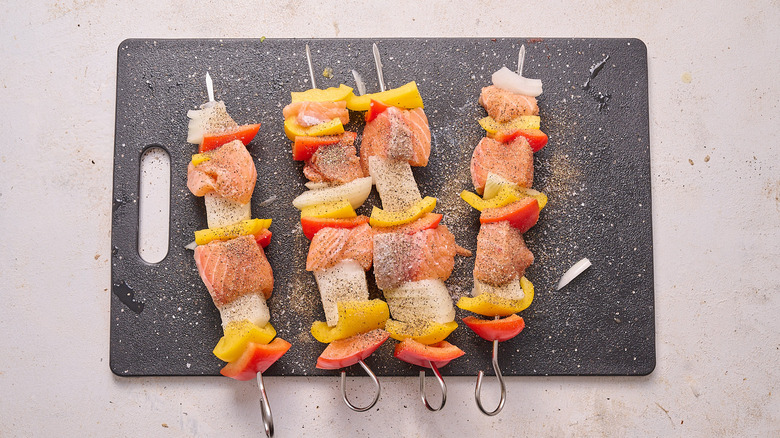 raw and seasoned salmon skewers on a cutting board