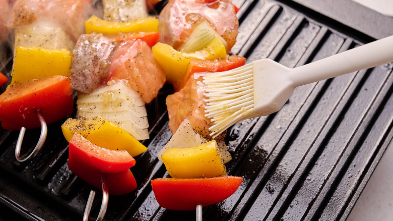 closeup of basting brush applying glaze onto salmon kebabs on a grill