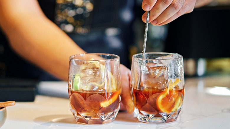 Someone mixing two glasses of ice and tea at a bar