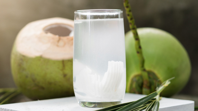 A glass of coconut water with two coconuts