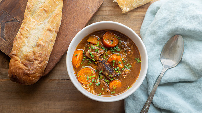 A comforting bowl of beef stew is paired with sliced carrots and potato