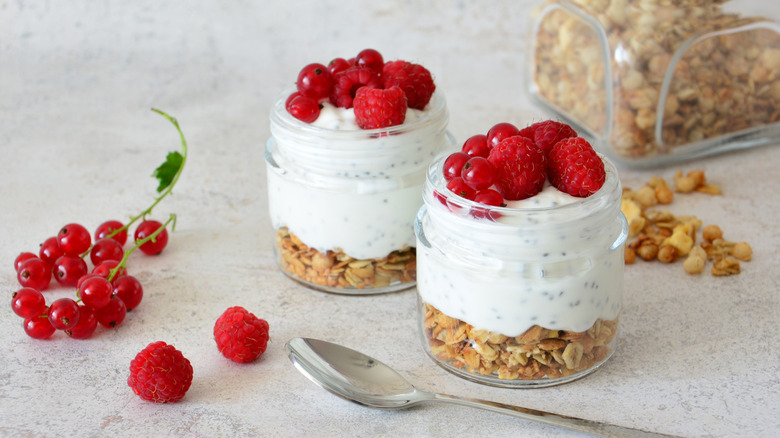 A glass cup of yogurt with whole raspberries on top with granola