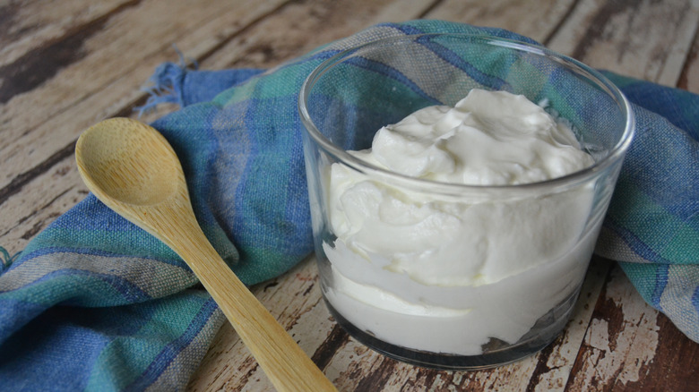 A glass cup of yogurt with a wooden spoon next to it.