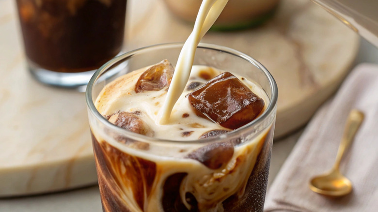 milk being poured into a glass of iced coffee