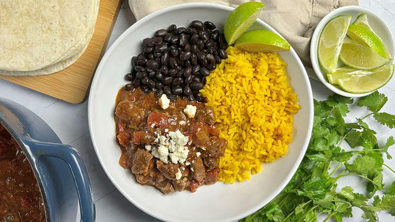 Slow-cooked carne picada beef stew in a bowl with rice, black beans, and lime wedges