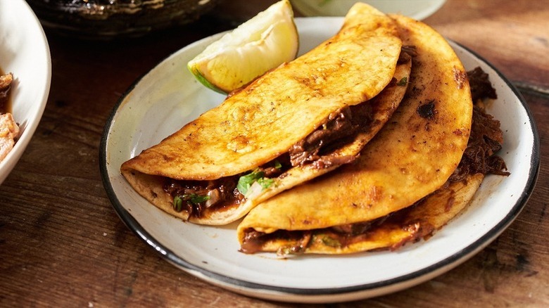 Slow-cooked birria beef tacos on a plate with a lime wedge