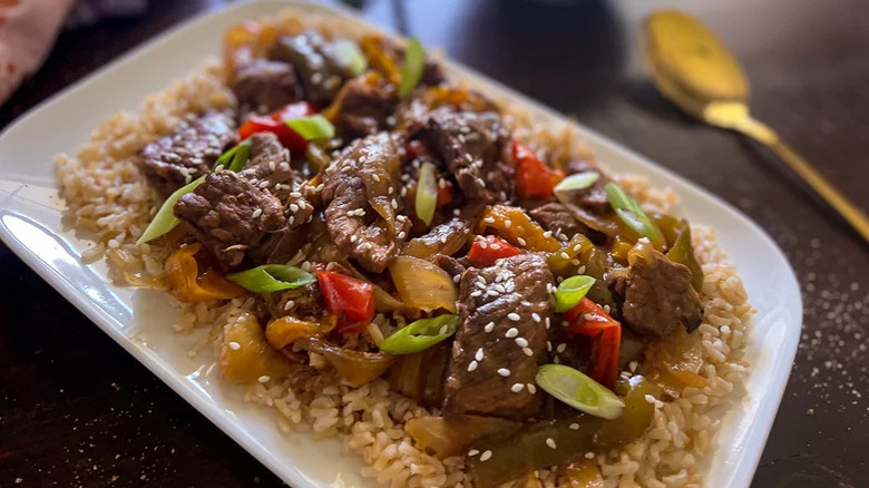 Chopped pepper steak on a plate with rice, red bell peppers, and chopped green onion