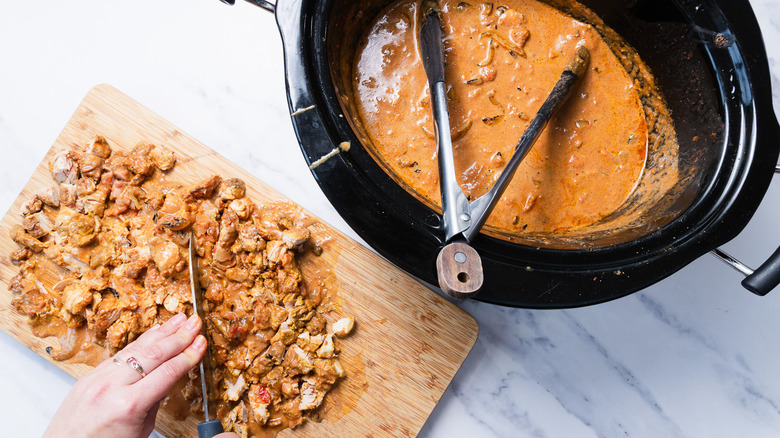 Chopping chicken on cutting board beside slow cooker