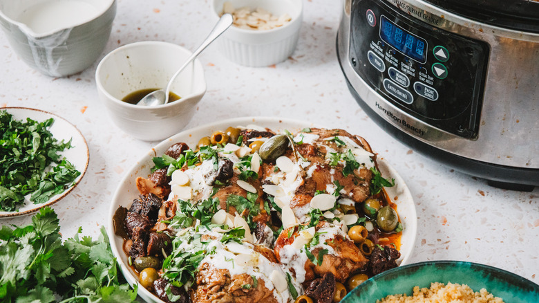 Large plate with bone-in chicken thighs with olives, figs, yogurt and cilantro, surrounded by more toppings and a slow cooker with chicken parts
