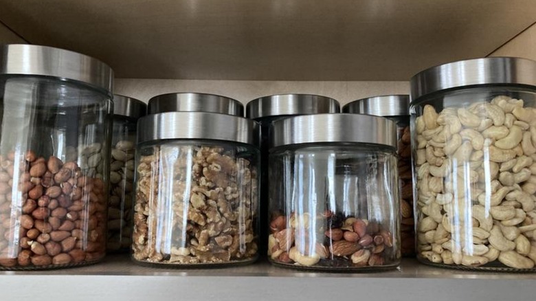 Different nuts sit in glass jars with stainless steel lids.