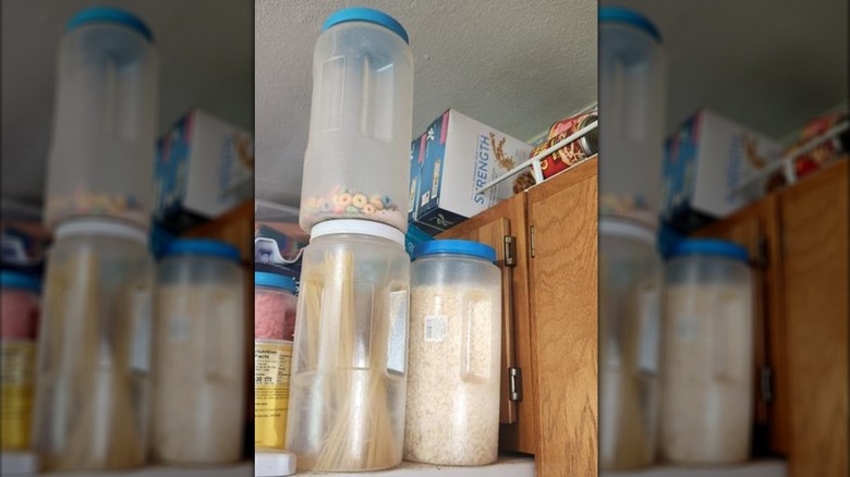 Three plastic canisters with twist-on lids sit in a kitchen filled with cereal and pasta.