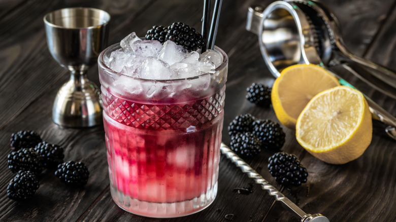 Bramble cocktail with blackberries, lemon, and jigger in background