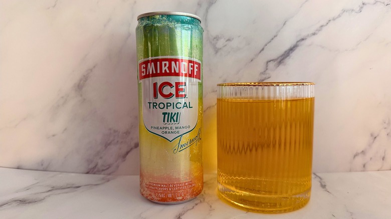 Can of Tropical Tiki Smirnoff Ice next to glass of Smirnoff Ice on marble surface