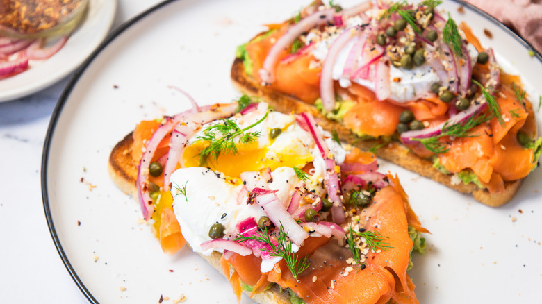 Two slices of smoked salmon breakfast toast with runny yolks on white plate.