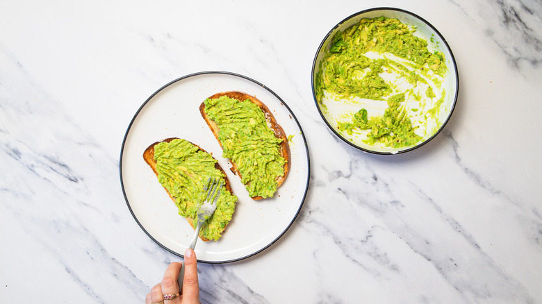Spreading avocado on two pieces of toast.