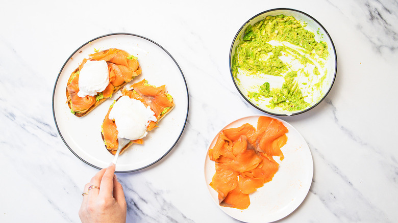 Laying poached egg on toast with avocado and smoked salmon.