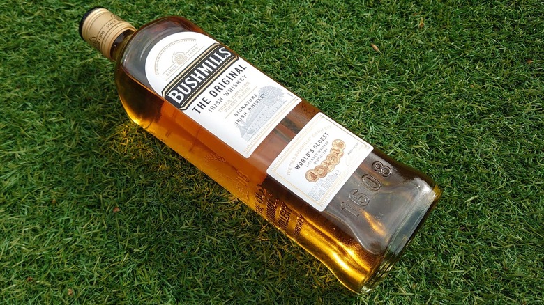 A bottle of Bushmills Original laid on artificial grass with the sunlight shining through