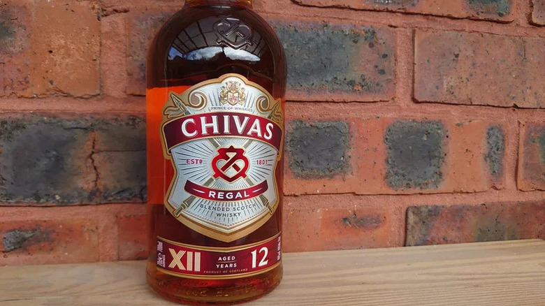 A close-up shot of a bottle of Chivas Regal 12-year in front of a red brick background