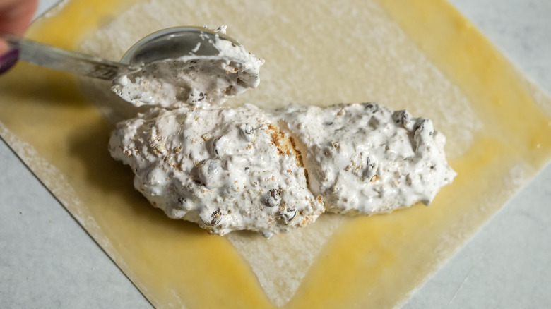 hand putting creamy white filling on egg roll wrapper