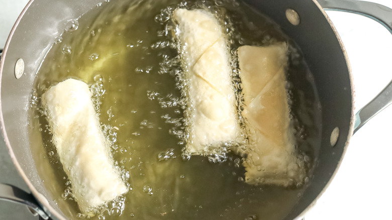 uncooked egg rolls in pot of oil
