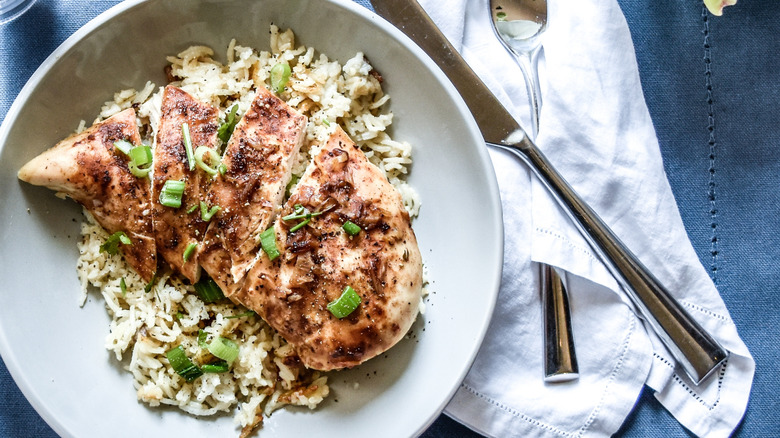 A bowl with French onion baked chicken on a bed of rice, next to a knife and fork on a napkin