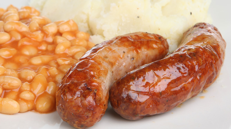 a closeup shot of bangers, mash, and beans together on a white plate