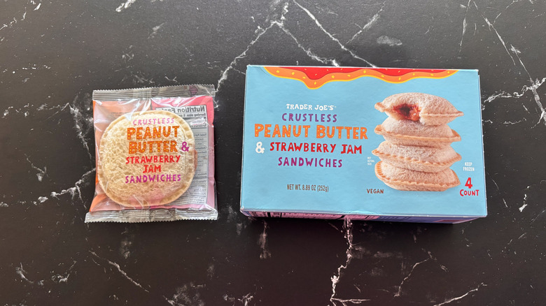 Trader Joe's crustless peanut butter and strawberry jam sandwiches box next to wrapped sandwich displayed on a black marbled counter