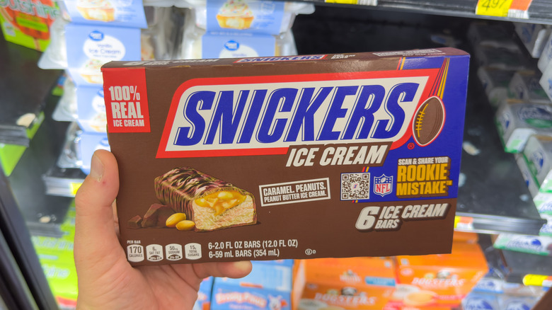 A hand holds a Snickers ice cream bar box.