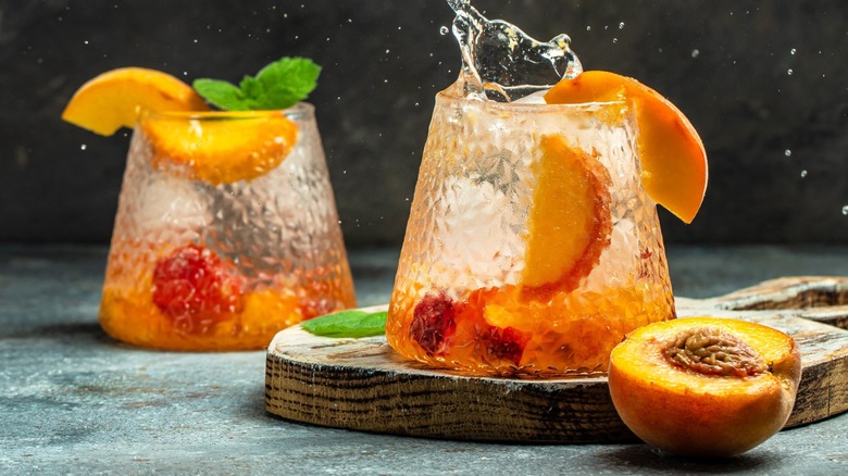 Two peach and bourbon cocktails with sliced peaches