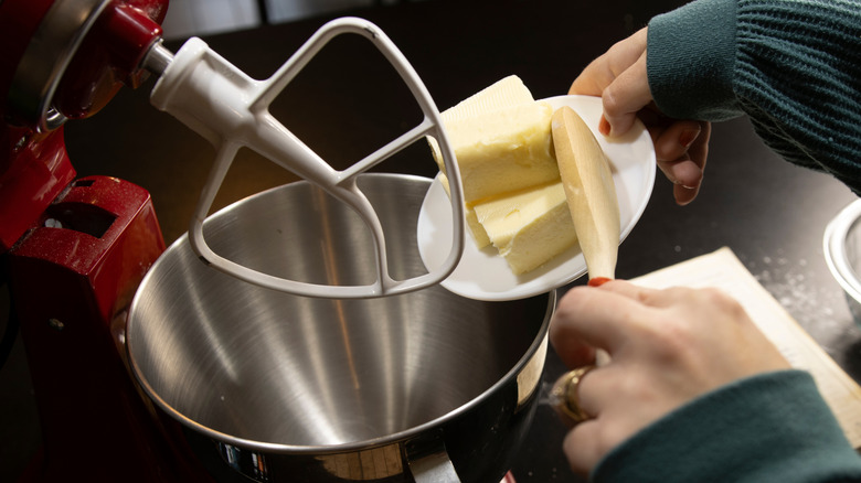 A person scrapes butter into a stand mixer