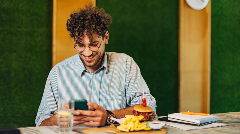 Person looking at their phone while eating alone at a restaurant