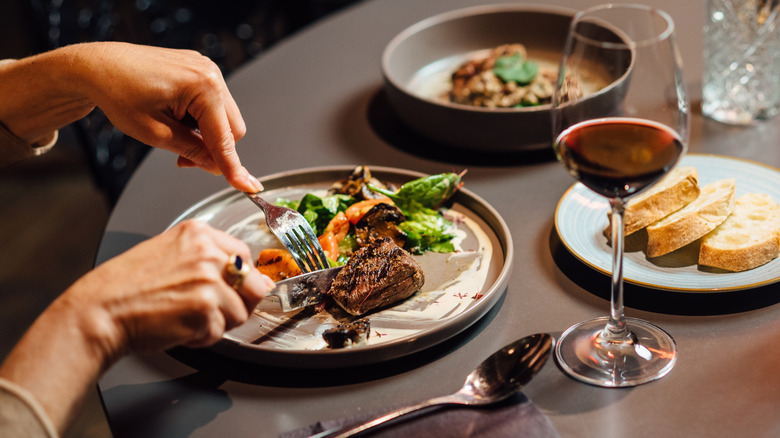 Hands cutting a piece of steak at a restaurant