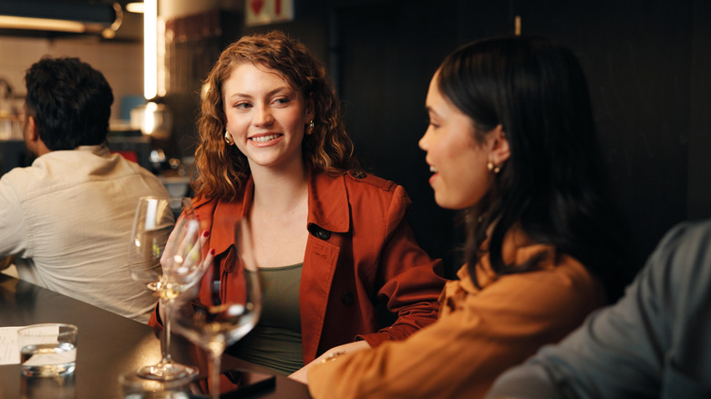 Two people talking at a restaurant bar with wine glasses