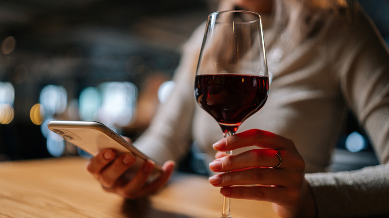 Person holding a glass of red wine and a phone at a restaurant