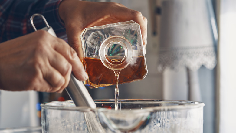 person pouring liquor into dish with ingredients for cooking