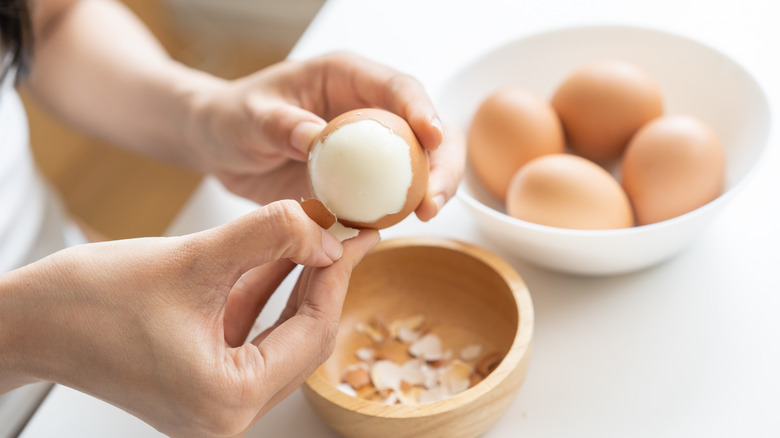 peeling boiled egg with bowl of hard boiled eggs in background