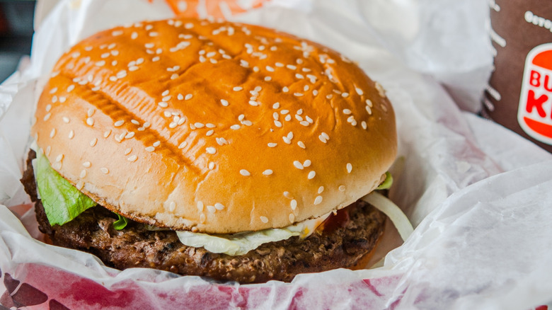 An unwrapped Burger King burger is sitting on its wrapper.