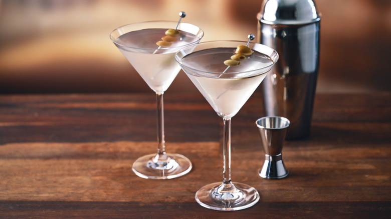 Two garnished martinis on a wooden table next to a shaker