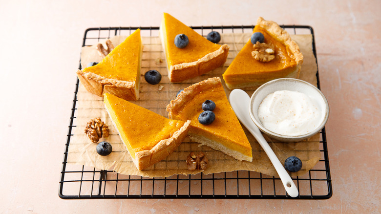 Slices of pumpkin pie with fresh berries, nuts, and sour cream