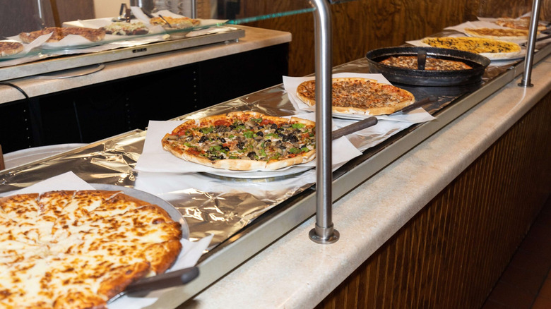 A buffet Line featuring at least seven different pizzas with serving utensils