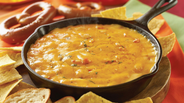 Beer cheese dip in skillet, surrounded by tortilla chips and pretzels