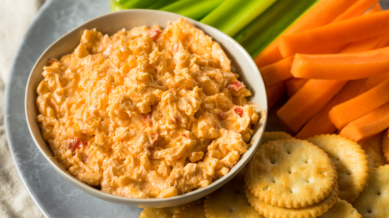 Bowl of pimento cheese dip next to crackers and crudites on plate