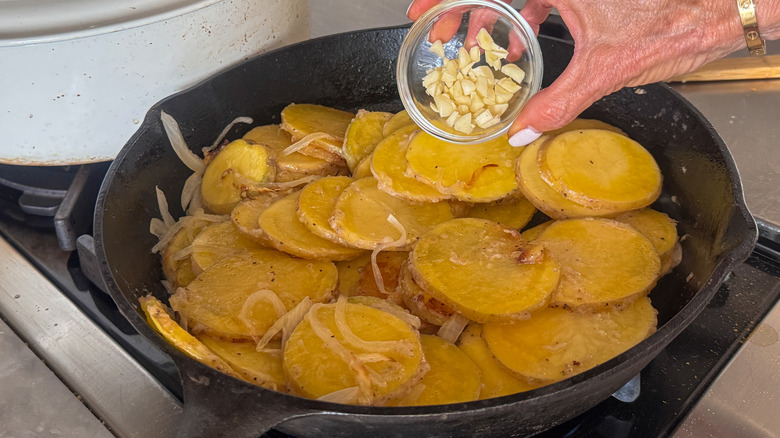 hand adding garlic to pan