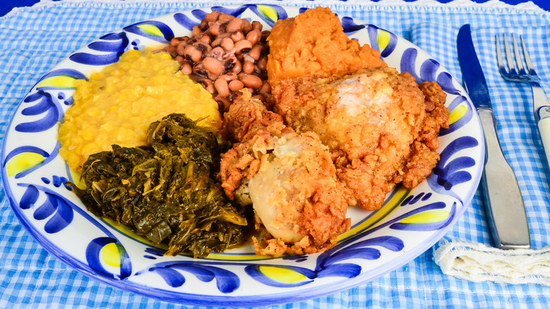 A plate of Soul Food featuring Fried Chicken, Black Eyed Peas, greens, some kind of puree on a blue gingham tablecloth